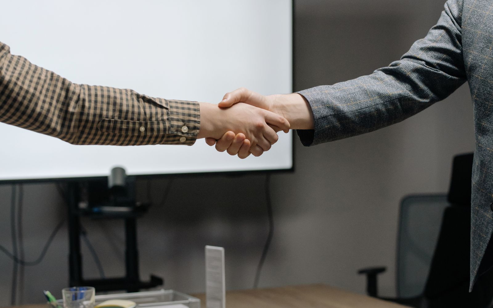 Two people shaking hands across a desk in a meeting room